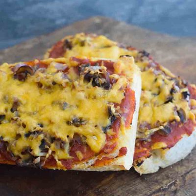 Two Air Fryer French Bread Pizzas on a cutting board, one leaning on the other.