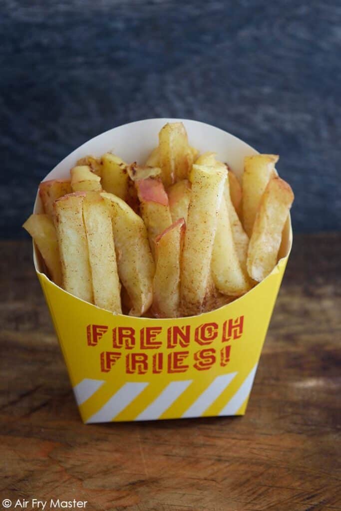 Air Fryer Apple Fries in a french fry carton, sitting on a wooden table.