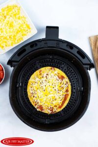 The uncooked Air Fryer Copycat Taco Bell Mexican Pizza sitting in an air fryer basket.