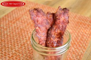 The finished air fryer bacon sitting upright in a canning jar.