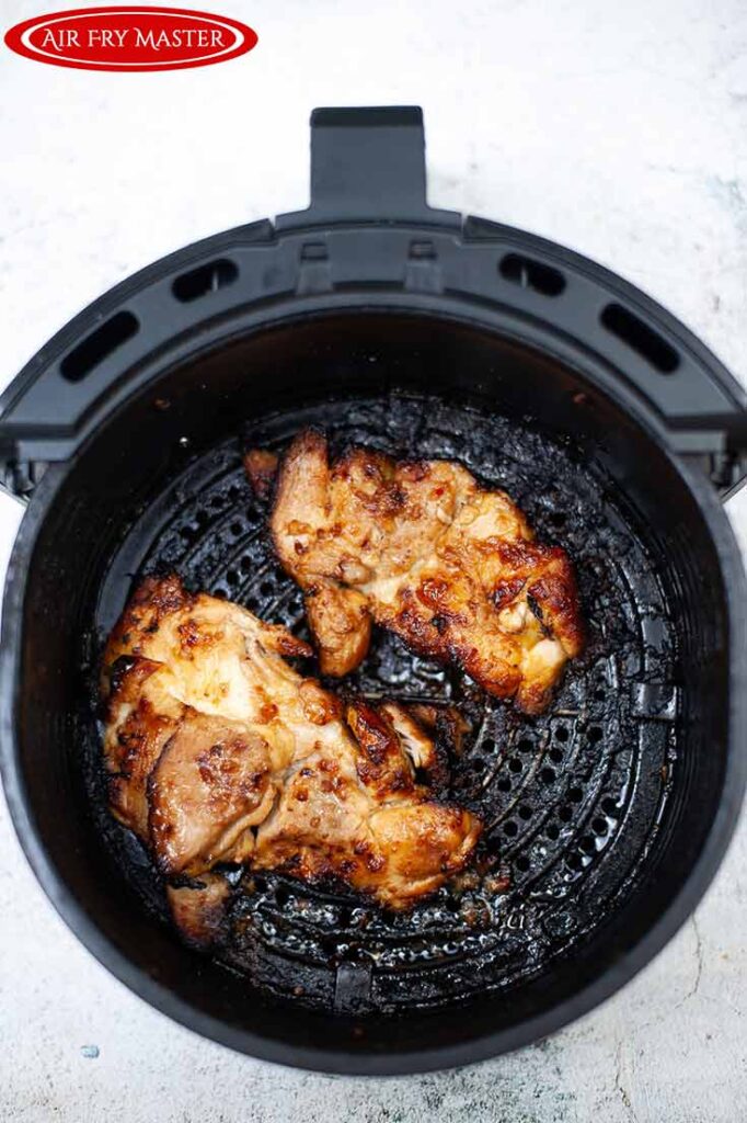 Two cooked pieces of chicken sitting in an air fryer basket.