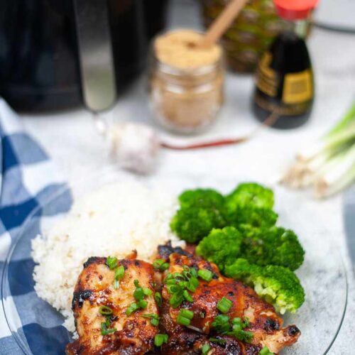 Two pieces of Air Fryer Huli Huli Chicken on a glass plate with a side of rice and broccoli.