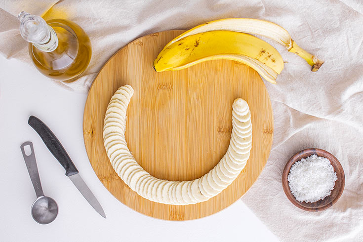 A banana sliced on a round, wooden cutting board.