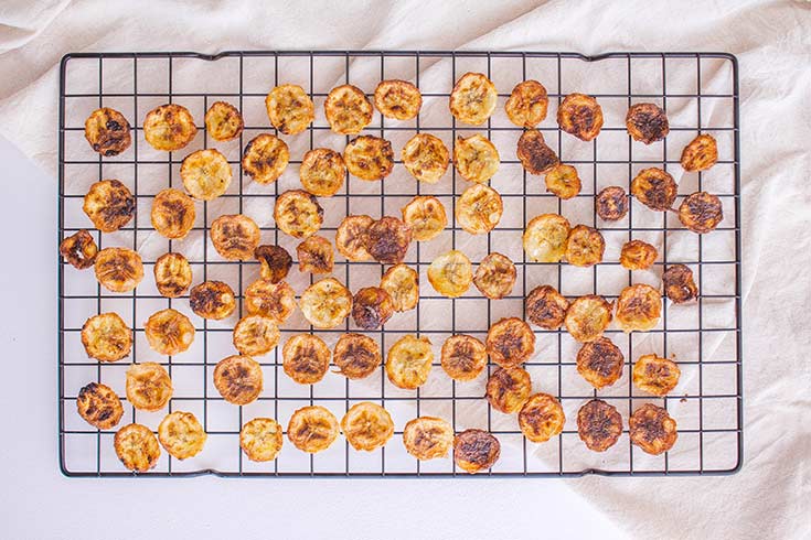 Air Fryer Banana Chips spread out over a black, wire, cooling rack to cool.