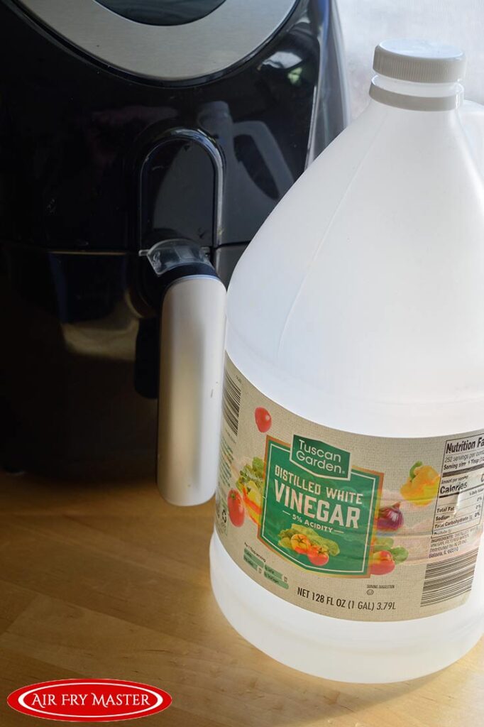 A large bottle of white vinegar sits next to a black air fryer.