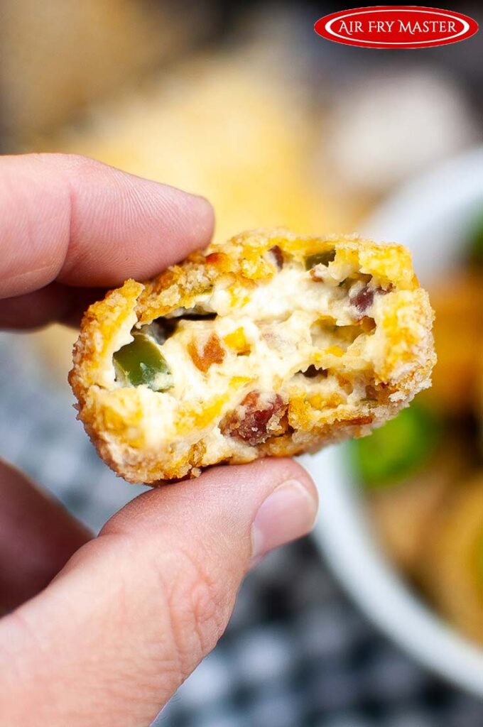 A single Air Fryer Jalapeño Popper Bite held to the camera with a bite missing so you can see the cheesy inside.